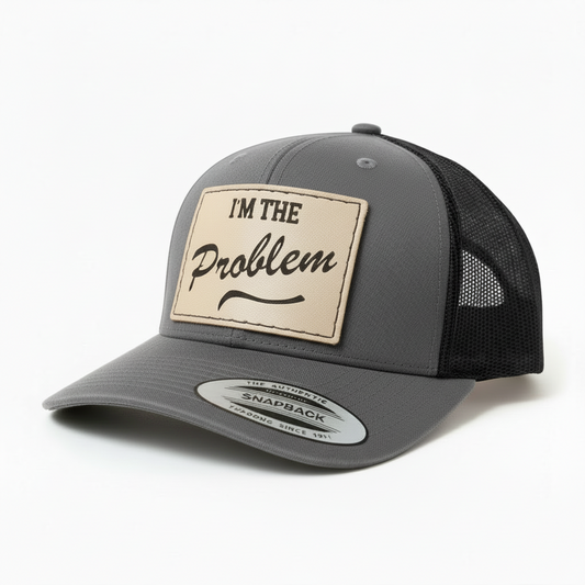 Black trucker cap with a beige patch that says 'I'm the Problem' on a white background