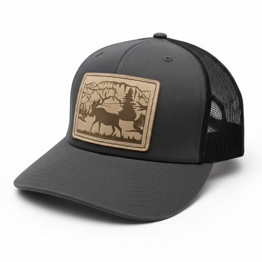 Gray trucker hat with a brown leather patch featuring a deer and forest design on a light gray background.