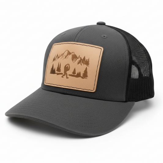 Gray trucker cap with a brown leather patch featuring a bear and mountains on a white background