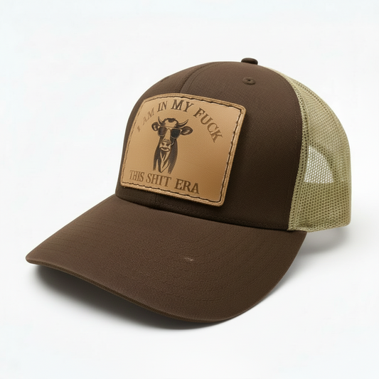 Brown trucker cap with a tan patch featuring text and a cow illustration on a white background
