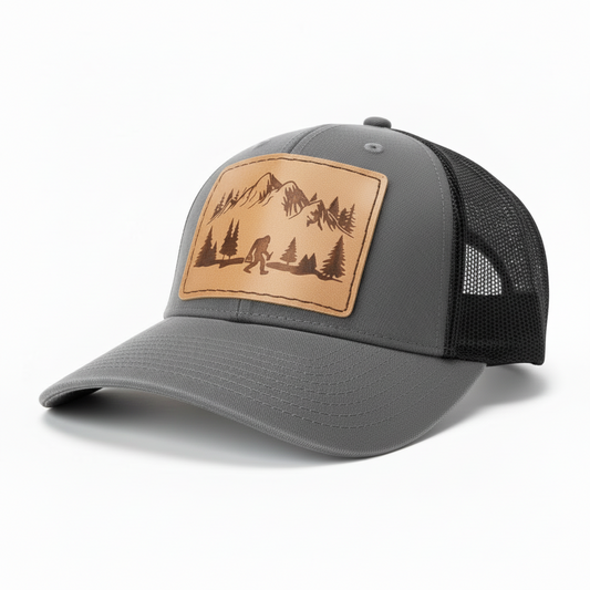 Black trucker cap with a leather patch featuring mountains and trees on a white background