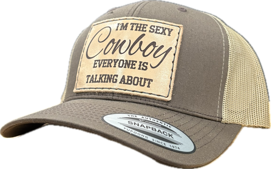 Brown and beige cap with a patch reading 'I'm the sexy cowboy everyone is talking about' on a white background.