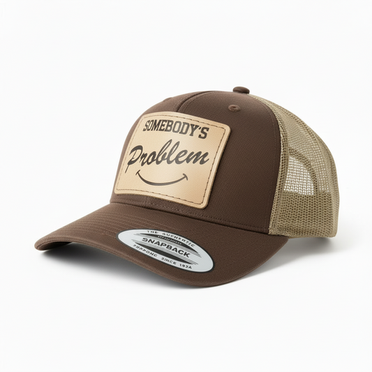 Gray and black trucker cap with leather patch and 'Somebody's Problem' text on a white background