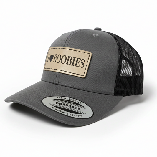 Black trucker cap with a tan patch displaying 'I ❤️ Boobies' on a white background