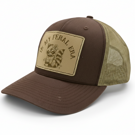 Brown and beige cap with 'In My Feral Era' patch on a light gray background