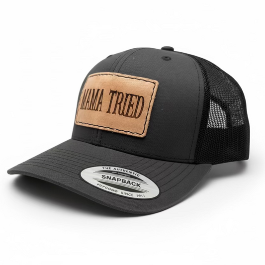 Black trucker cap with a brown leather patch labeled 'Mama Tried' on a light gray background