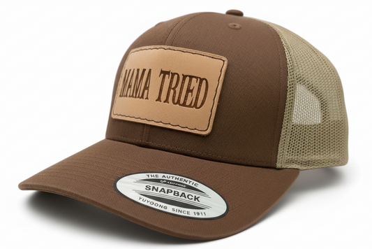 Black trucker cap with a brown leather patch and 'MAMA TRIED' text on a light gray background.