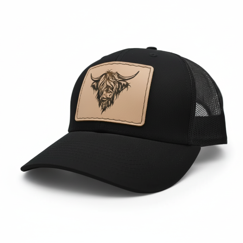 Black trucker cap with a tan patch featuring a highland cow design on a white background
