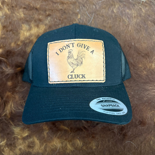 Black cap with a rooster patch and text on a brown textured background