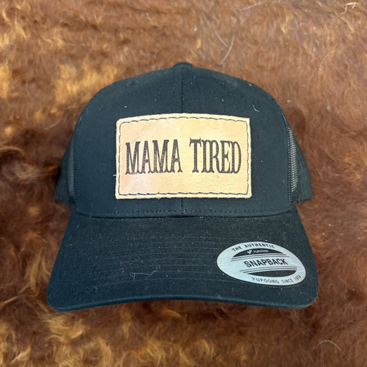 Black cap with 'MAMA TIRED' patch on a brown textured background