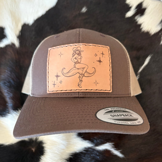 Brown and beige cap with a leather patch featuring a cowboy design on a cowhide background