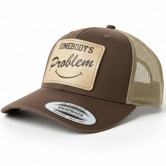 Gray and black trucker cap with leather patch and 'Somebody's Problem' text on a white background